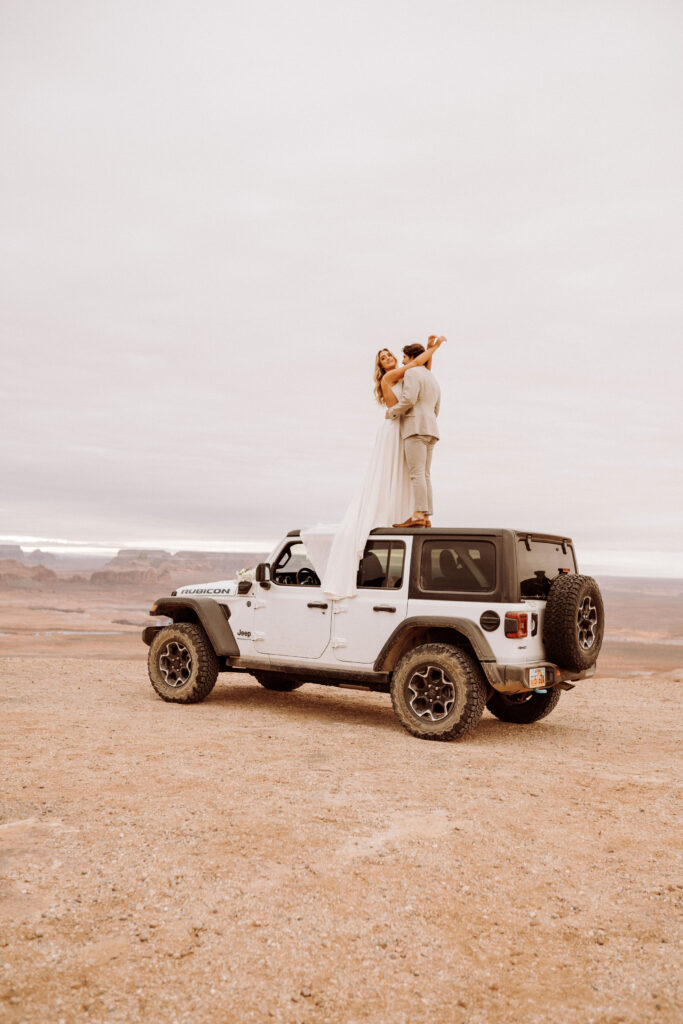 celebrating their elopement by standing on the top of the jeep embracing each other 